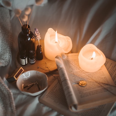 Image of a cozy arrangement of candles, essential oils, a reed diffuser, and an open paperback book