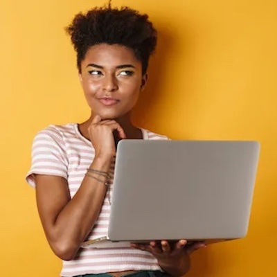 An African American woman in thought while holding an open laptop.